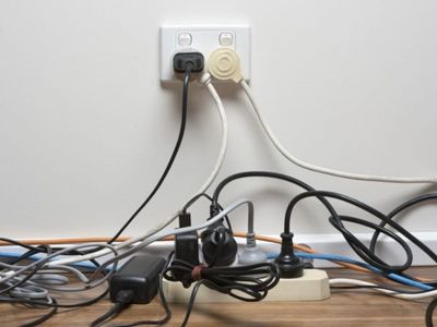 Overloaded electrical outlet with multiple cords and plugs, illustrating the dangers of circuit overloads and electrical safety tips for homeowners.