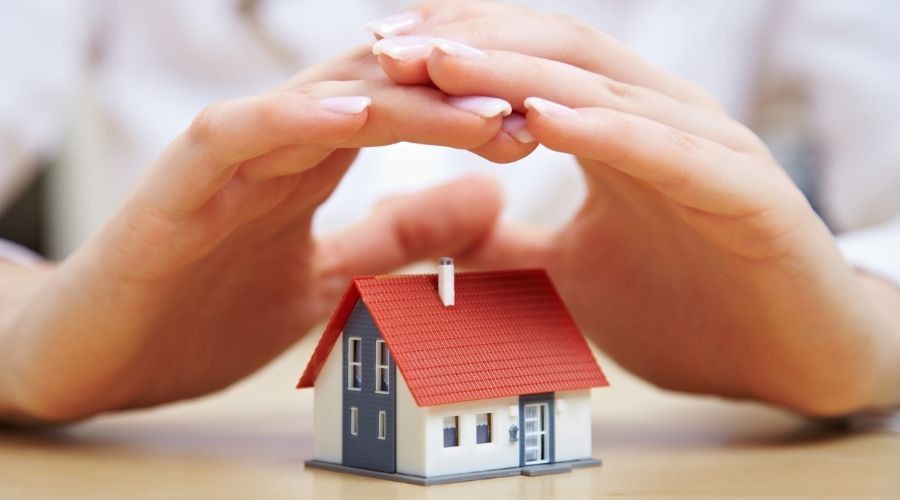 Hands protecting a miniature house model, symbolizing whole-home surge protection and electrical safety for homeowners.