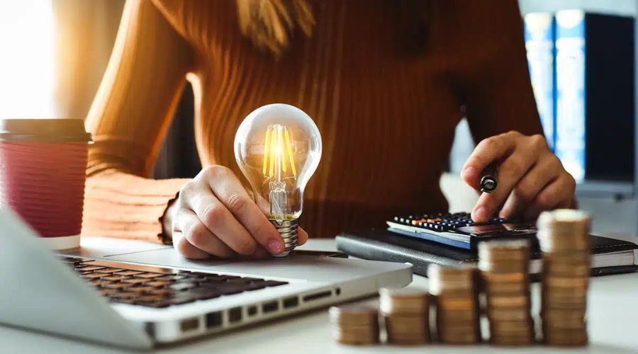 Person analyzing energy savings with a light bulb and calculator, emphasizing cost-effective LED lighting upgrades for homes.