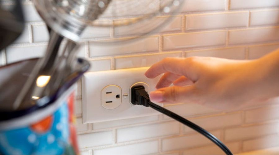 Hand plugging in an electrical cord into a wall outlet, emphasizing safe electrical practices in home environments.