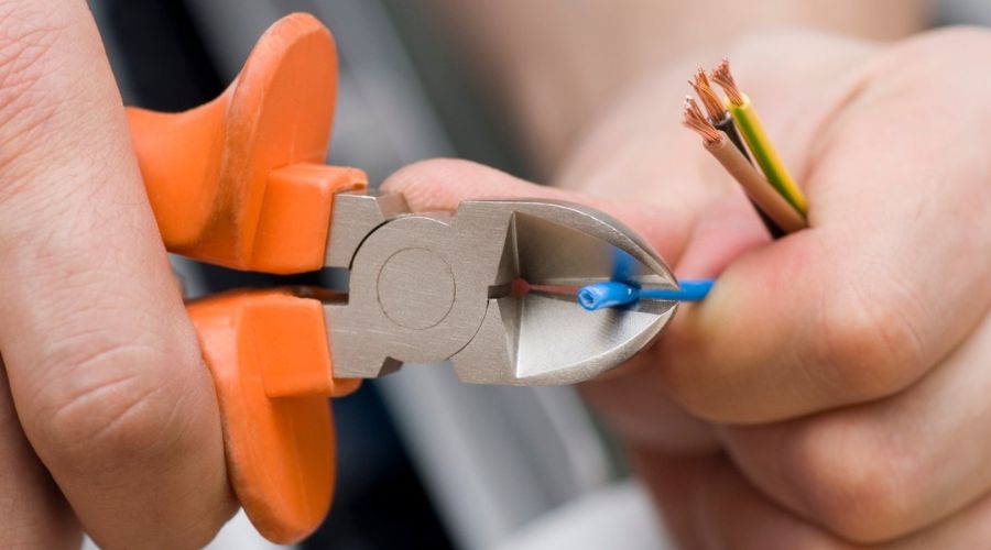 Hands using wire cutters to trim electrical wires, illustrating electrical upgrades and DIY projects for summer home improvements.