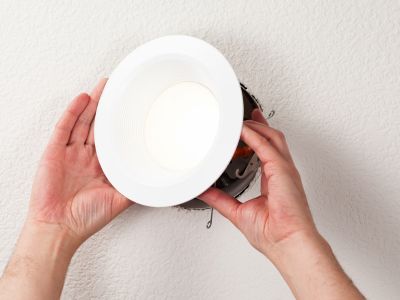 Hands installing a recessed LED light fixture into a ceiling, illustrating home electrical upgrades for improved lighting efficiency.