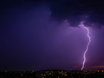 Lightning striking during a storm over a city skyline, illustrating potential causes of power outages that a standby generator can mitigate.